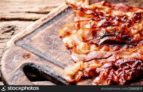 Fried bacon on a cutting board. On a wooden background. High quality photo. Fried bacon on a cutting board.