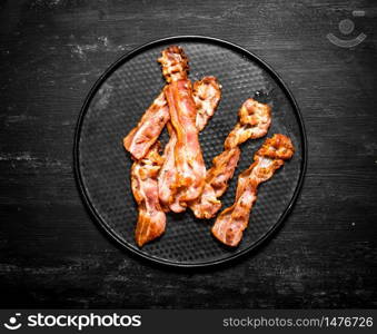 Fried bacon on a plate. On a black wooden background.. Fried bacon on a plate.
