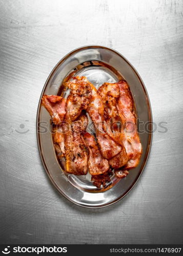 Fried bacon on a plate. On the Metal table.. Fried bacon on a plate.