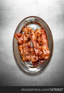 Fried bacon on a plate. On the Metal table.. Fried bacon on a plate.