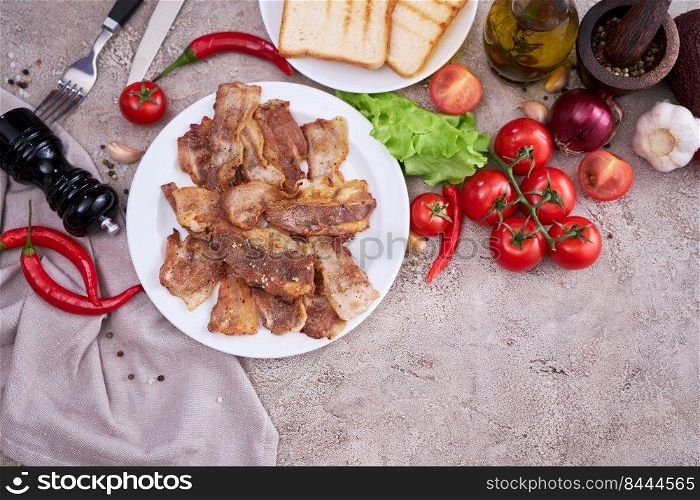 fried bacon pieces in a plate and vegetables at domestic kitchen stone or concrete table.. fried bacon pieces in a plate and vegetables at domestic kitchen stone or concrete table