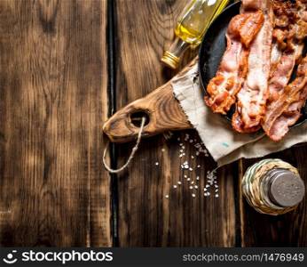Fried bacon with salt in a frying pan on the Board. On a wooden table.. Fried bacon with salt
