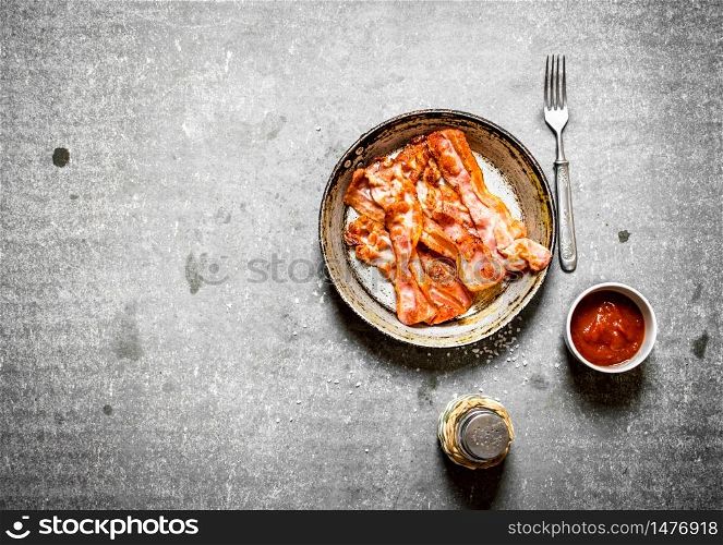 Fried bacon with tomato sauce and salt. On a stone background.. Fried bacon with tomato sauce and salt.