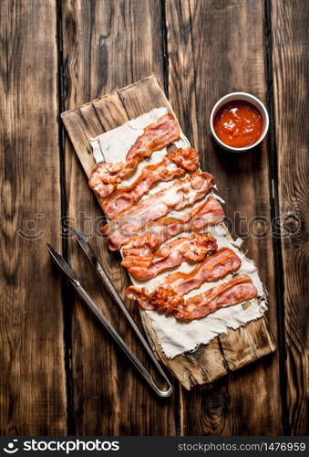 Fried bacon with tomato sauce. On a wooden background.. Fried bacon with tomato sauce. On wooden background.