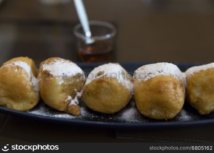 fried banana dessert topping with icing sugar on black dish serving with honey, selective focus