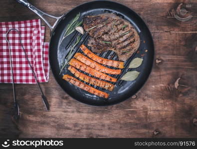 fried beef stack and fried carrots on a round frying pan, brown wooden background, top view