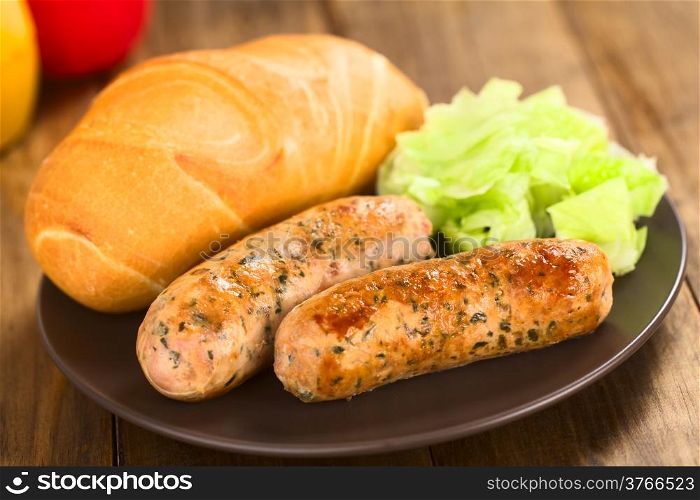 Fried bratwurst with bun, traditional German fast food served on plate with green salad (Selective Focus, Focus on the right side of the right bratwurst)