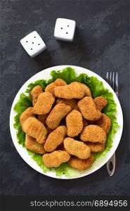 Fried breaded crispy chicken nuggets on lettuce leaves on plate, photographed overhead on slate with natural light. Chicken Nuggets