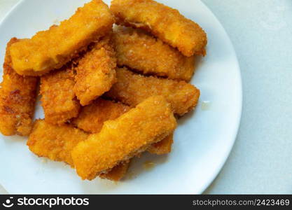 Fried brown fish fingers on a white plate, top view