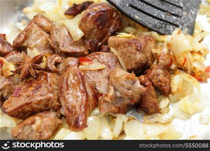 fried brown lamb cubes in a pan with onions, star anise, ginger, and garlic, part of the preparation of a far-eastern style curry