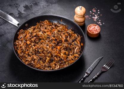 Fried ch&ignons with carrots, onions and spices in a pan against a dark concrete background. Vegetarian cuisine. Fried ch&ignons with carrots, onions and spices in a pan against a dark concrete background