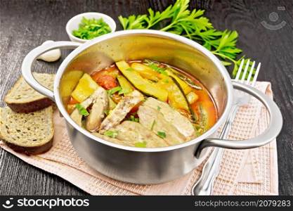 Fried chicken breast slices with stewed zucchini, tomatoes and garlic in a saucepan on napkin, bread, parsley and a fork on wooden board background