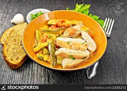 Fried chicken breast slices with stewed zucchini, tomatoes and garlic in a plate, bread, parsley and a fork on wooden board background