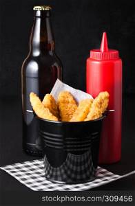 Fried chicken dippers in black bucket with sauce and beer bottle on black background