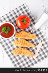 Fried chicken dippers on chopping board with sauce and tomato on paper background.Top view
