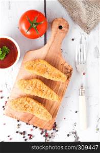 Fried chicken dippers on chopping board with sauce and tomato on wooden background