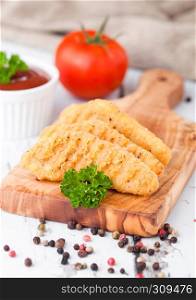 Fried chicken dippers on chopping board with sauce and tomato on wooden background