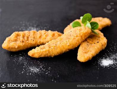 Fried chicken dippers on stone board with salt on black background