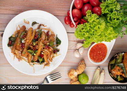 Fried Chicken Feet with Herbs on a white plate and dipping sauce with lemongrass, garlic, lemon and tomatoes on a wooden floor.