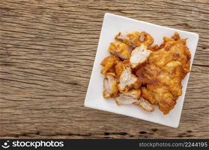 fried chicken in white square ceramic plate on rustic natural wood texture background with copy space for text, top view
