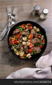 Fried chicken liver with vegetable side dish of tomatoes, carrots, mushrooms, peas in a pan