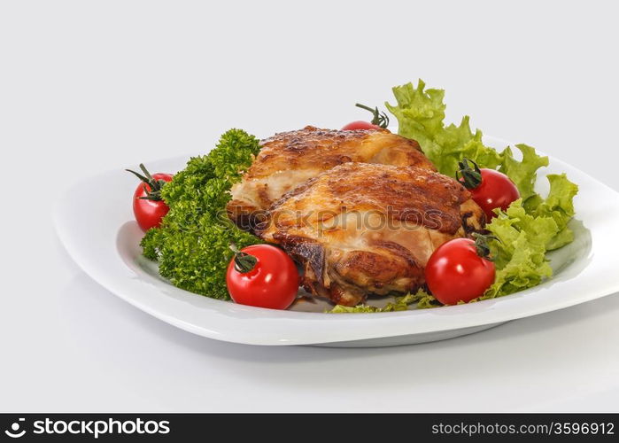 Fried chicken pieces on a plate with tomatoes, lettuce and parsley. Taken on a sheet of white plastic. Is not an isolate.