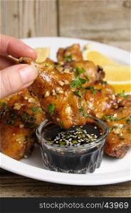 Fried chicken wing in ginger garlic marinade with herbs in hand over soy sauce