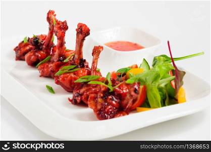 fried chicken wings fried in pomegranate sauce with vegetable salad on white plate. fried chicken wings in pomegranate sauce