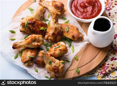 Fried chicken wings with sauces on wooden board, close up, selective focus, top view