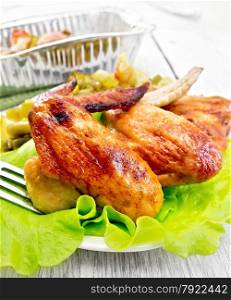 Fried chicken wings with vegetables and salad leaves on a plate, a fork, a form of foil on the background light wooden boards