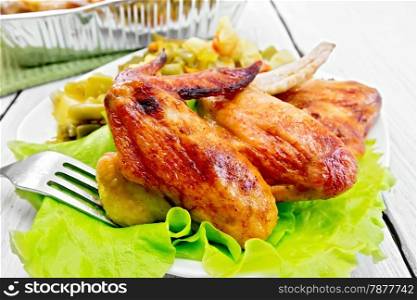 Fried chicken wings with vegetables and salad leaves on a plate, fork on the background light wooden boards