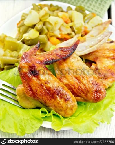 Fried chicken wings with vegetables and salad leaves on a plate, fork, napkin on the background light wooden boards