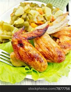 Fried chicken wings with vegetables and salad leaves on a plate, fork, napkin on the background light wooden boards