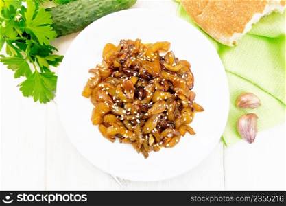 Fried cucumbers with garlic, honey, soy sauce and spices in a plate, bread, napkin and parsley on a wooden board background from above