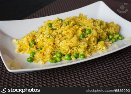 Fried curry rice with peas served on white plate at restaurant, brown background.