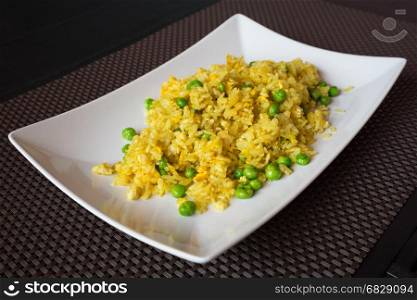 Fried curry rice with peas served on white plate at restaurant, brown background.