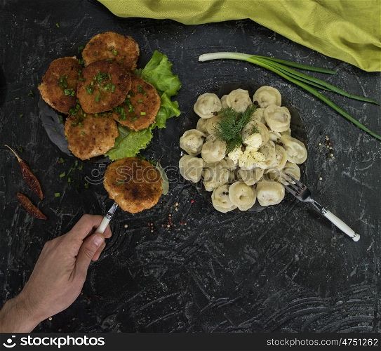 Fried cutlets and russian pelmeni on black background. Fried cutlets and russian pelmeni on black background. Food set. Top view.