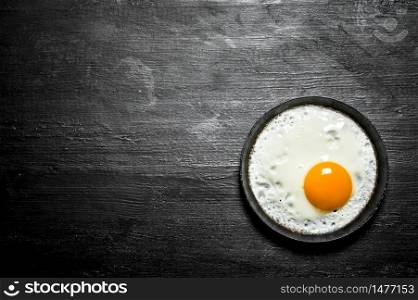 Fried egg in a frying pan. On a black wooden background.. Fried egg in a frying pan. On black wooden background.