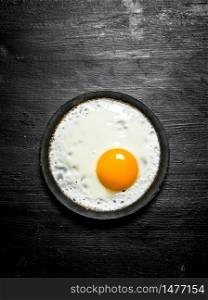 Fried egg in a frying pan. On a black wooden background.. Fried egg in a frying pan. On black wooden background.