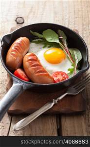 Fried egg sausages tomatoes in pan for breakfast