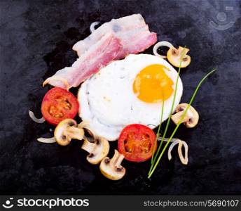 fried egg with bacon, mushrooms and vegetables on fried pan