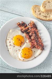 Fried eggs and bacon on the white plate on the wooden table