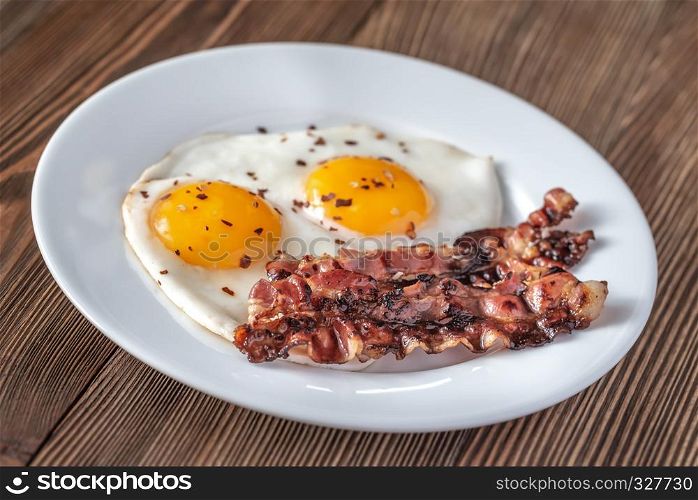 Fried eggs and bacon on the white plate on the wooden table