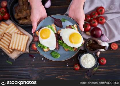 Fried eggs, bacon and cream cheese sandwiches on a plate on wooden table at domestic kitchen.. Fried eggs, bacon and cream cheese sandwiches on a plate on wooden table at domestic kitchen