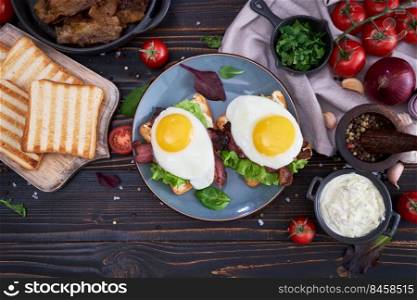 Fried eggs, bacon and cream cheese sandwiches on a plate on wooden table at domestic kitchen.. Fried eggs, bacon and cream cheese sandwiches on a plate on wooden table at domestic kitchen
