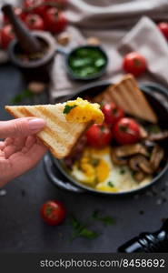 Fried eggs, bacon, tomato and toasted bread in a black ceramic pan at domestic kitchen.. Fried eggs, bacon, tomato and toasted bread in a black ceramic pan at domestic kitchen