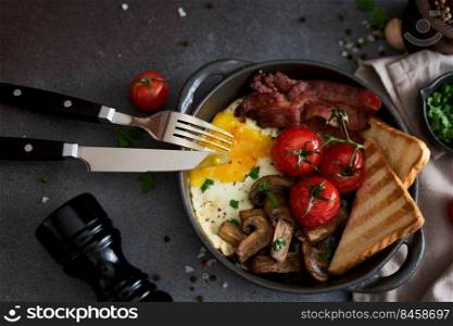 Fried eggs, bacon, tomato and toasted bread in a black ceramic pan at domestic kitchen.. Fried eggs, bacon, tomato and toasted bread in a black ceramic pan at domestic kitchen