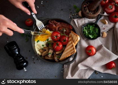 Fried eggs, bacon, tomato and toasted bread in a black ceramic pan at domestic kitchen.. Fried eggs, bacon, tomato and toasted bread in a black ceramic pan at domestic kitchen