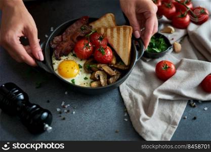Fried eggs, bacon, tomato and toasted bread in a black ceramic pan at domestic kitchen.. Fried eggs, bacon, tomato and toasted bread in a black ceramic pan at domestic kitchen