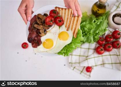 Fried eggs, bacon, tomato and toasted bread in white ceramic plate.. Fried eggs, bacon, tomato and toasted bread in white ceramic plate